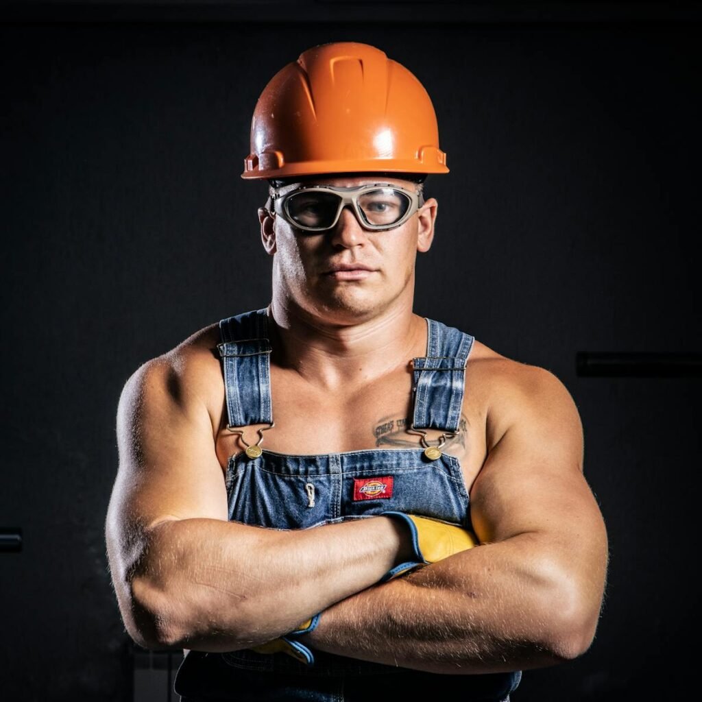 Portrait of a muscular construction worker with arms crossed, wearing goggles and a hard hat.